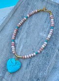 Pink opal necklace with turquoise heart pendant laid flat by the pool