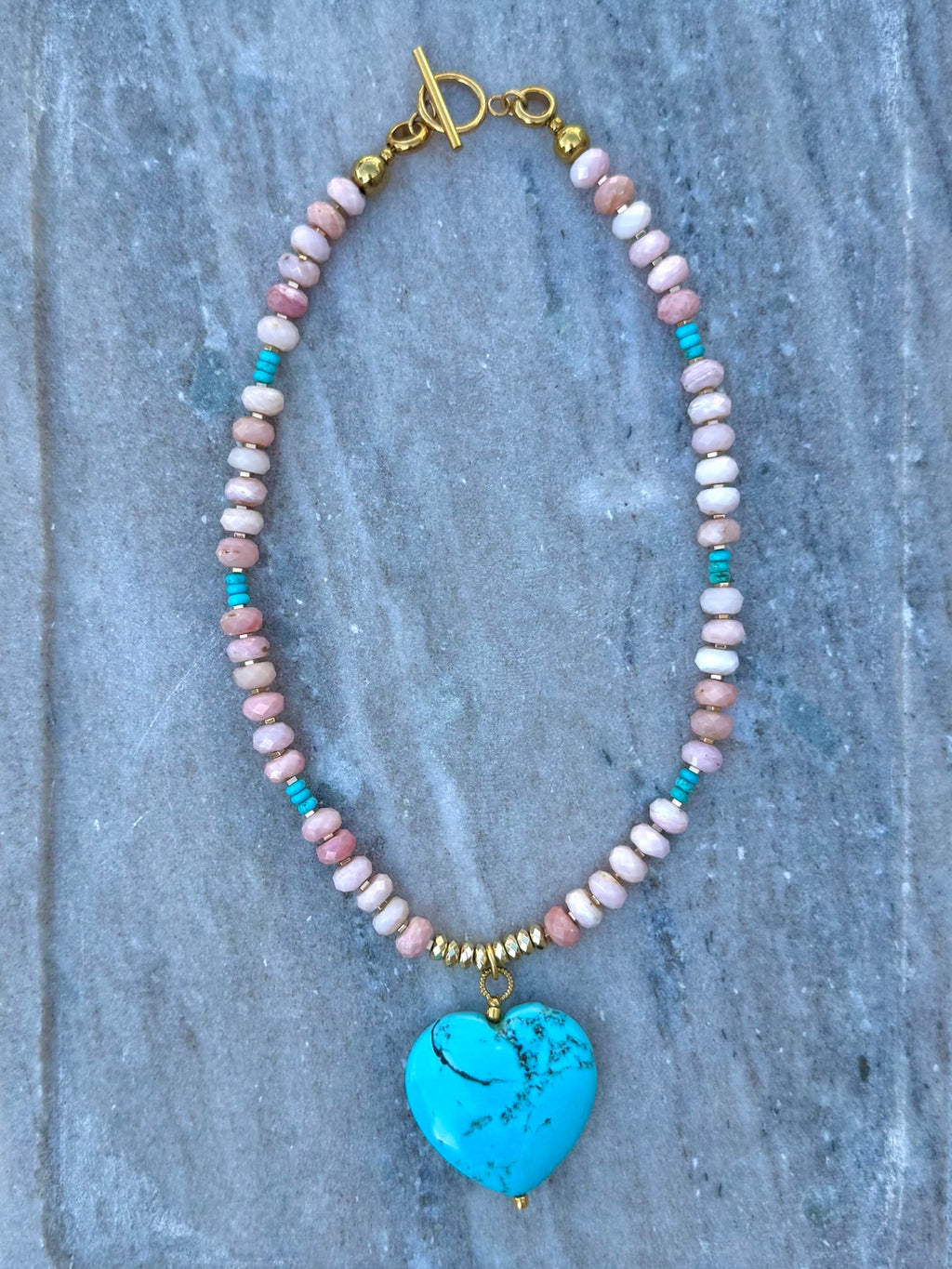 Straight-on poolside view of pink opal necklace with turquoise heart pendant