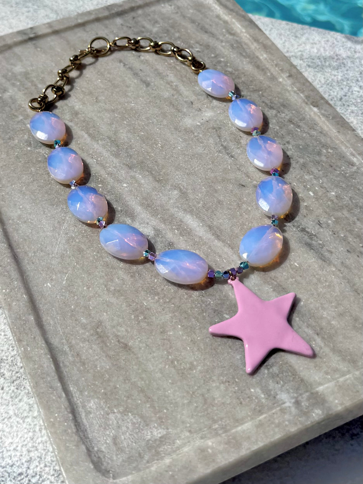 Angled poolside view of The Bonnie pink opal star necklace