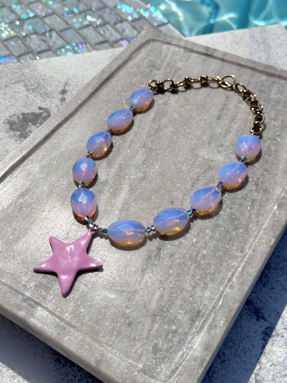 Close poolside view of The Bonnie pink opal star necklace
