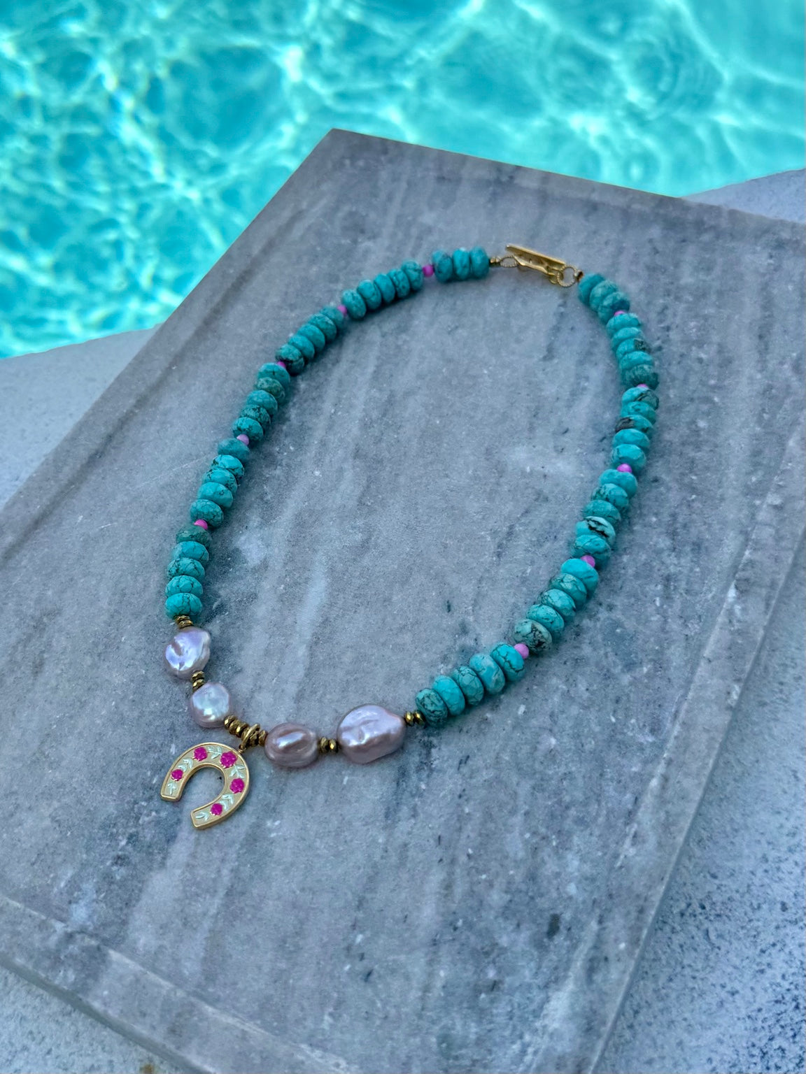 Angled poolside view of turquoise and purple pearl necklace with horseshoe charm