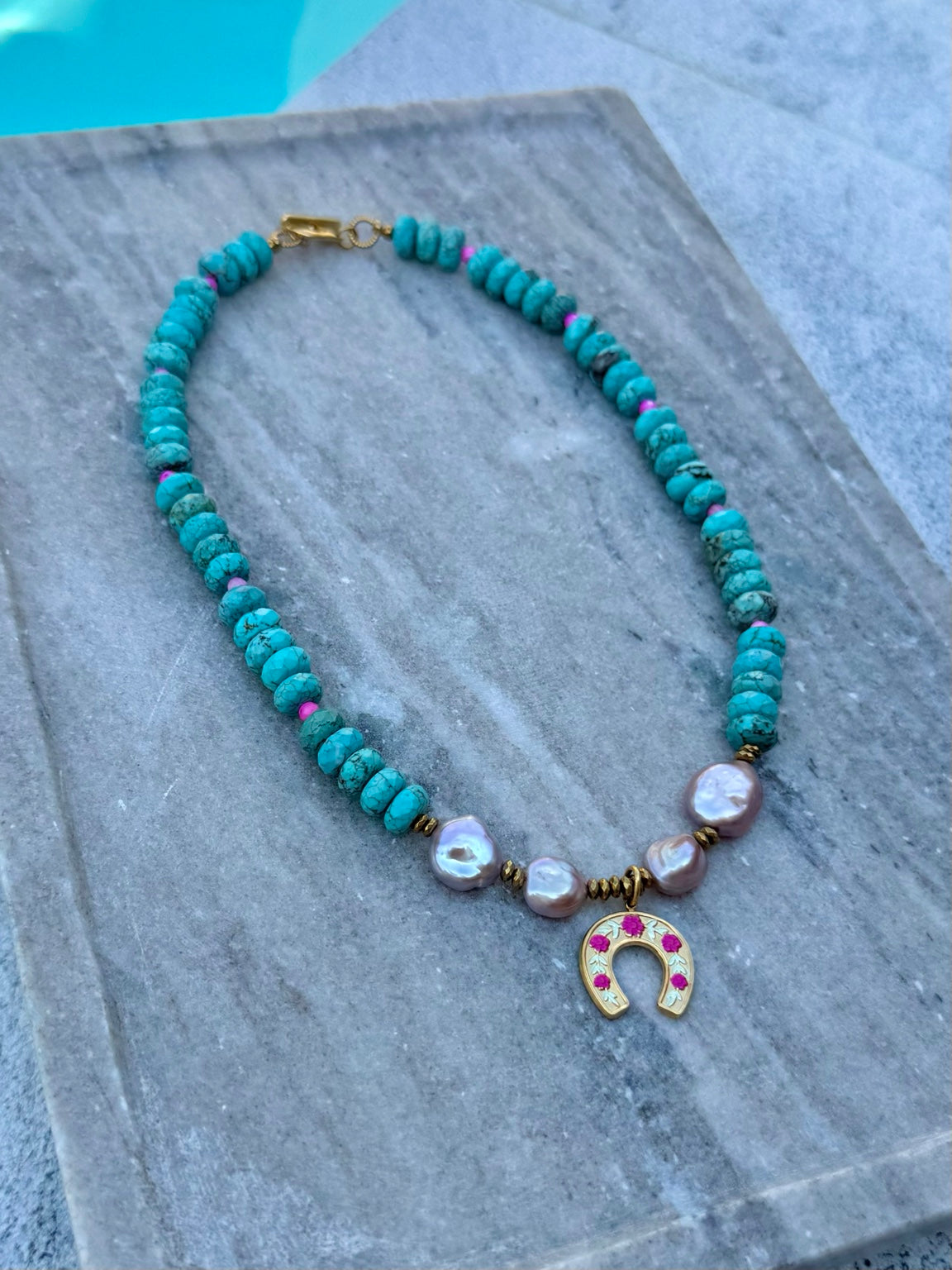 Close poolside view of turquoise necklace with purple freshwater pearls and gold horseshoe charm
