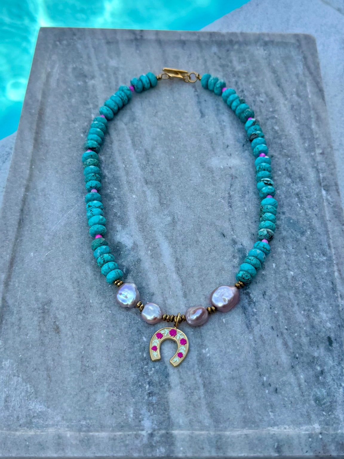 Turquoise and purple freshwater pearl necklace with gold horseshoe charm photographed poolside