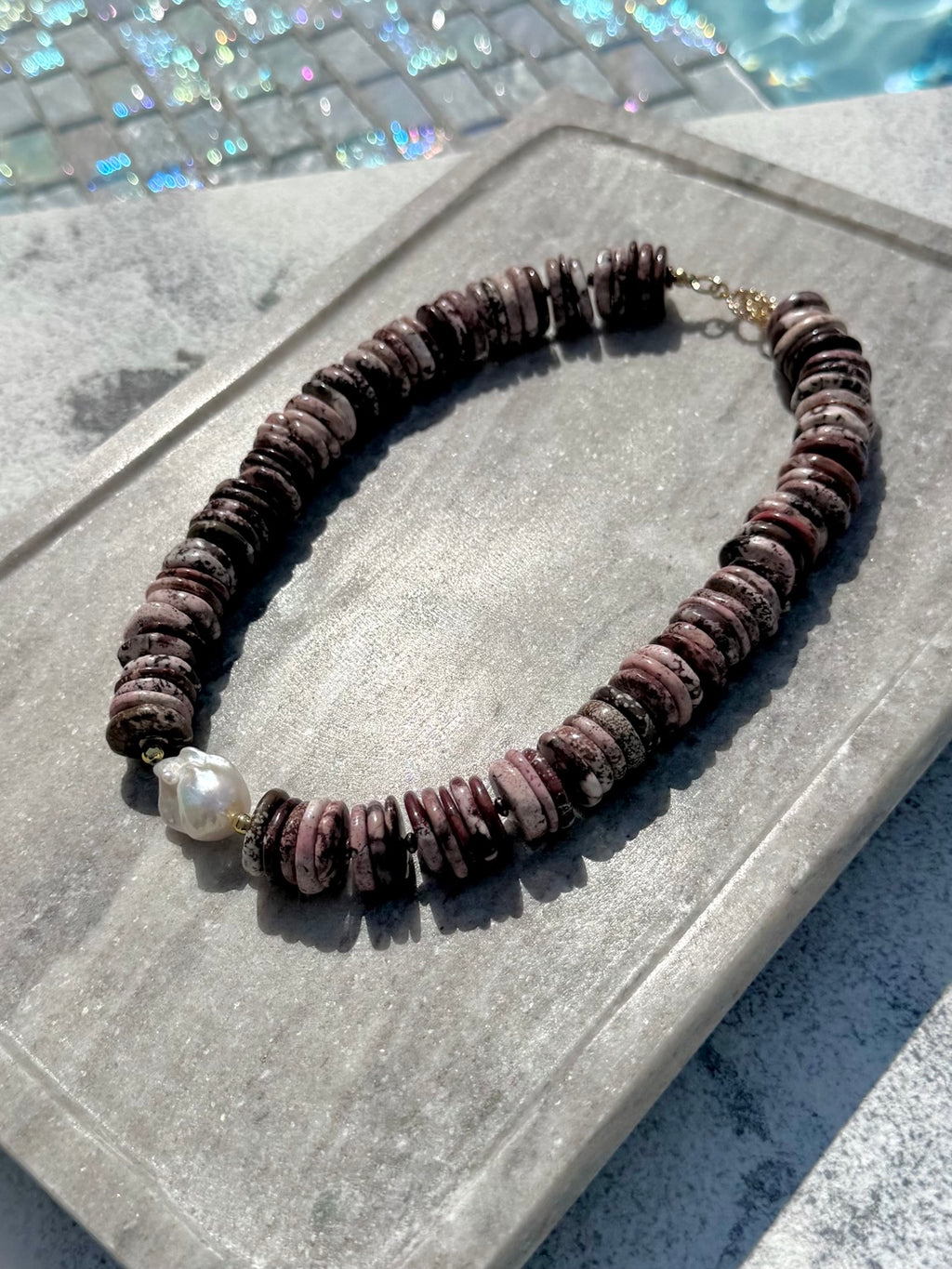 Angled poolside view of brown turquoise disc necklace with baroque pearl