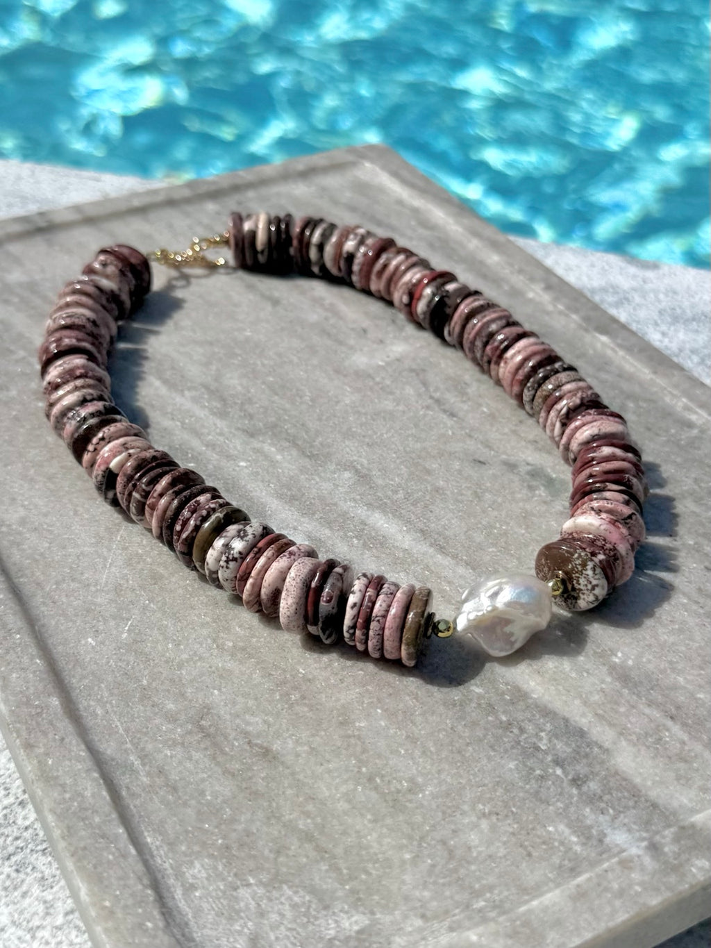 Close poolside view of brown turquoise disc necklace with baroque pearl
