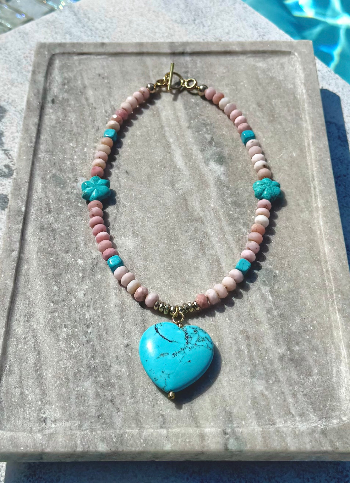 Poolside detail view of The Colt pink opal and turquoise flower heart necklace