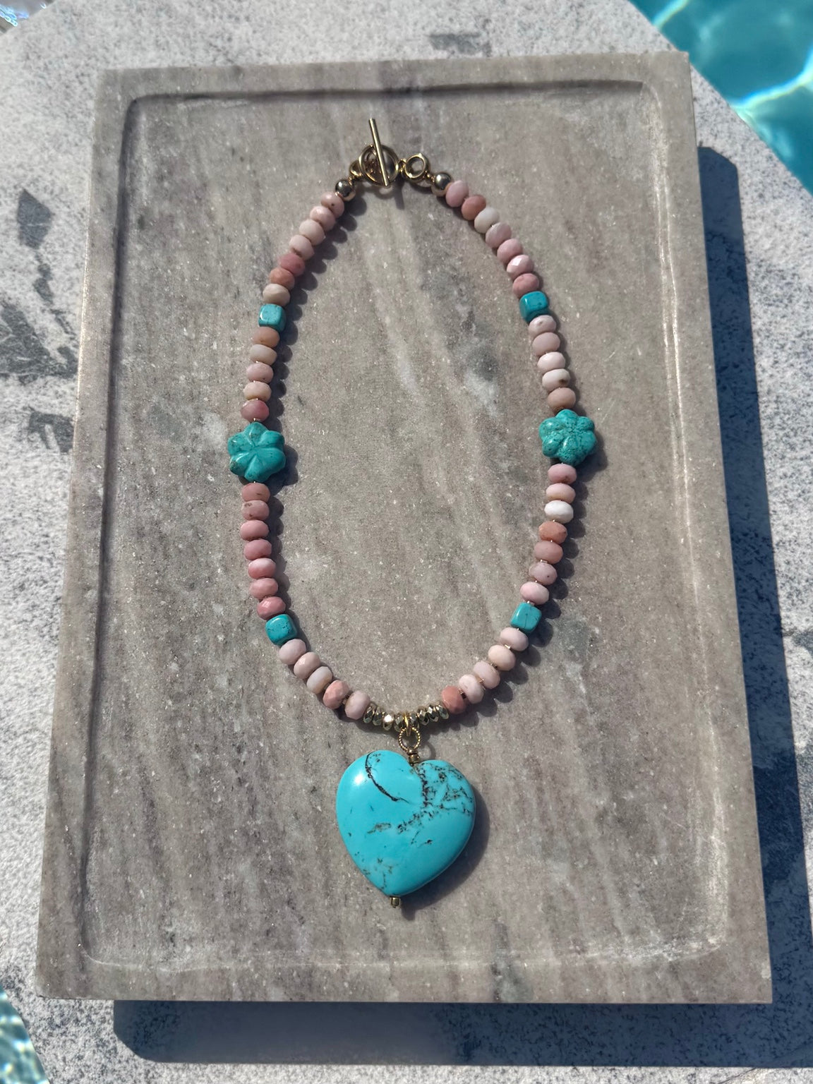 The Colt pink opal and turquoise flower heart necklace photographed poolside