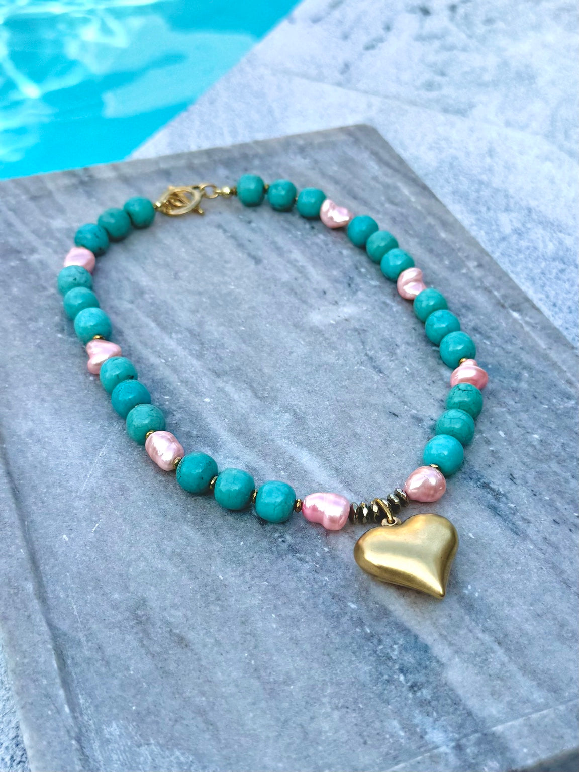 Angled poolside view of turquoise and pink pearl heart necklace
