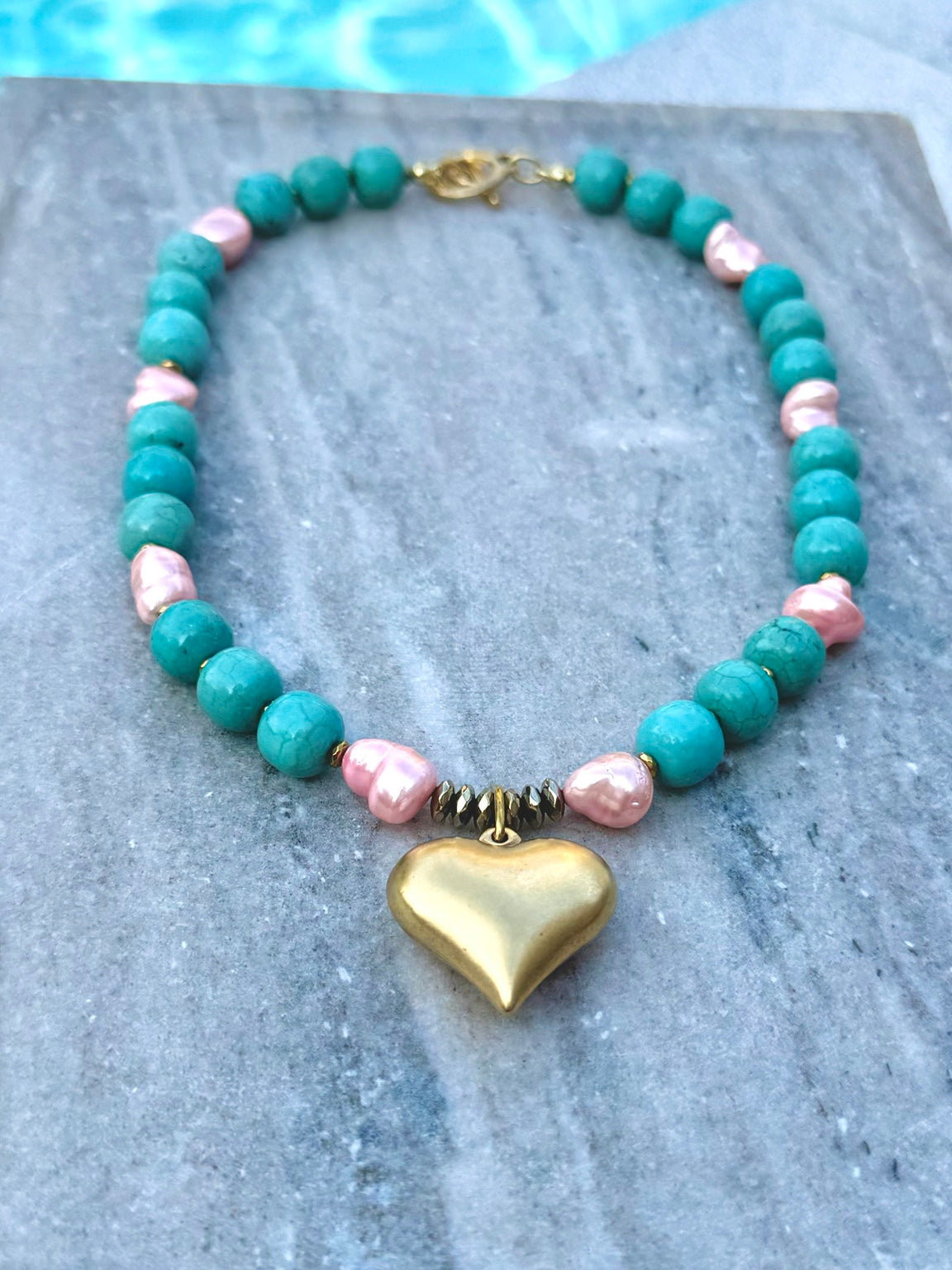 Turquoise and pink freshwater pearl necklace with gold heart charm photographed poolside
