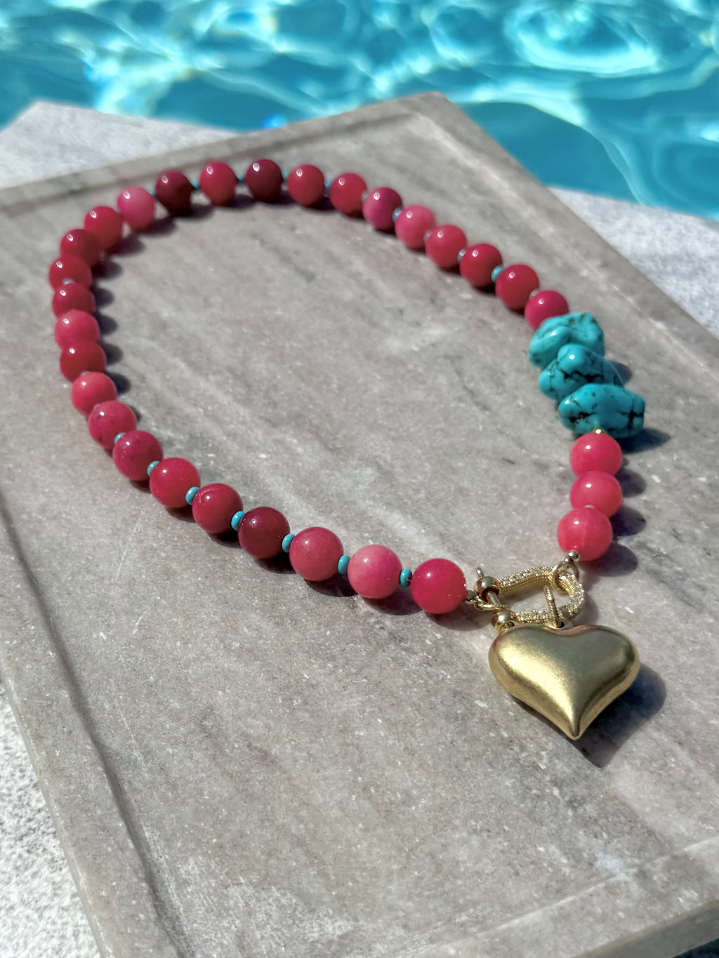 Angled poolside view of pink and turquoise necklace with gold heart charm