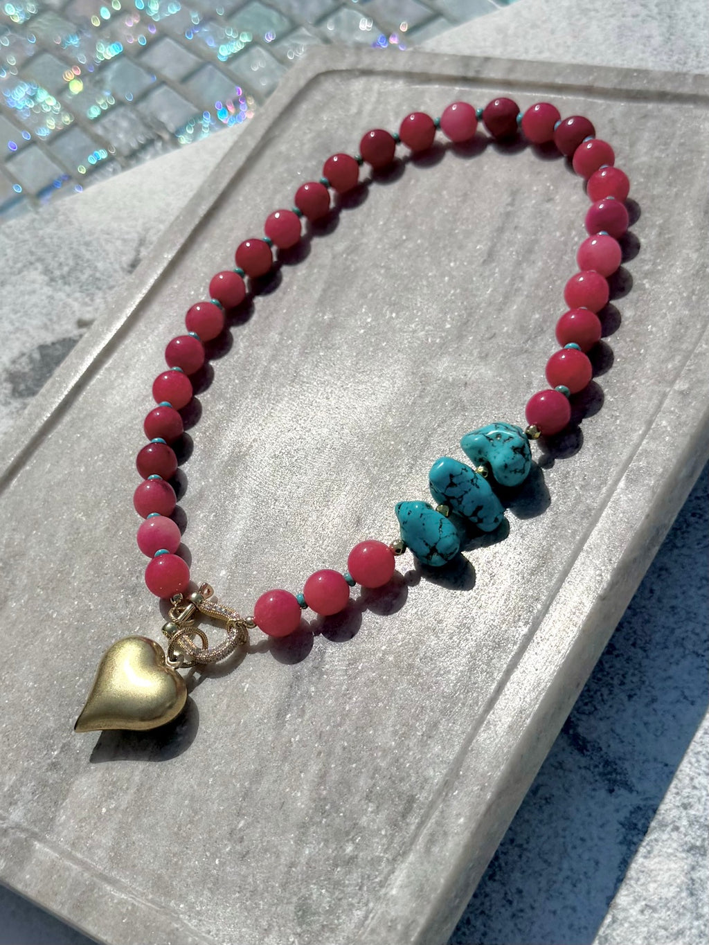 Pink bead necklace with turquoise nugget accents and gold heart charm photographed poolside