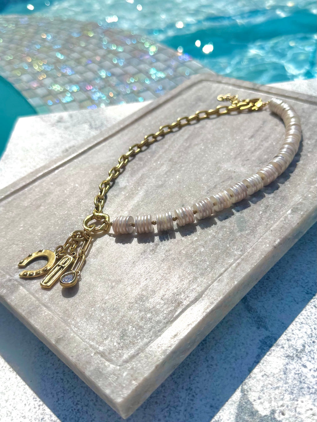 Angled poolside view of white shell disc and gold charm necklace