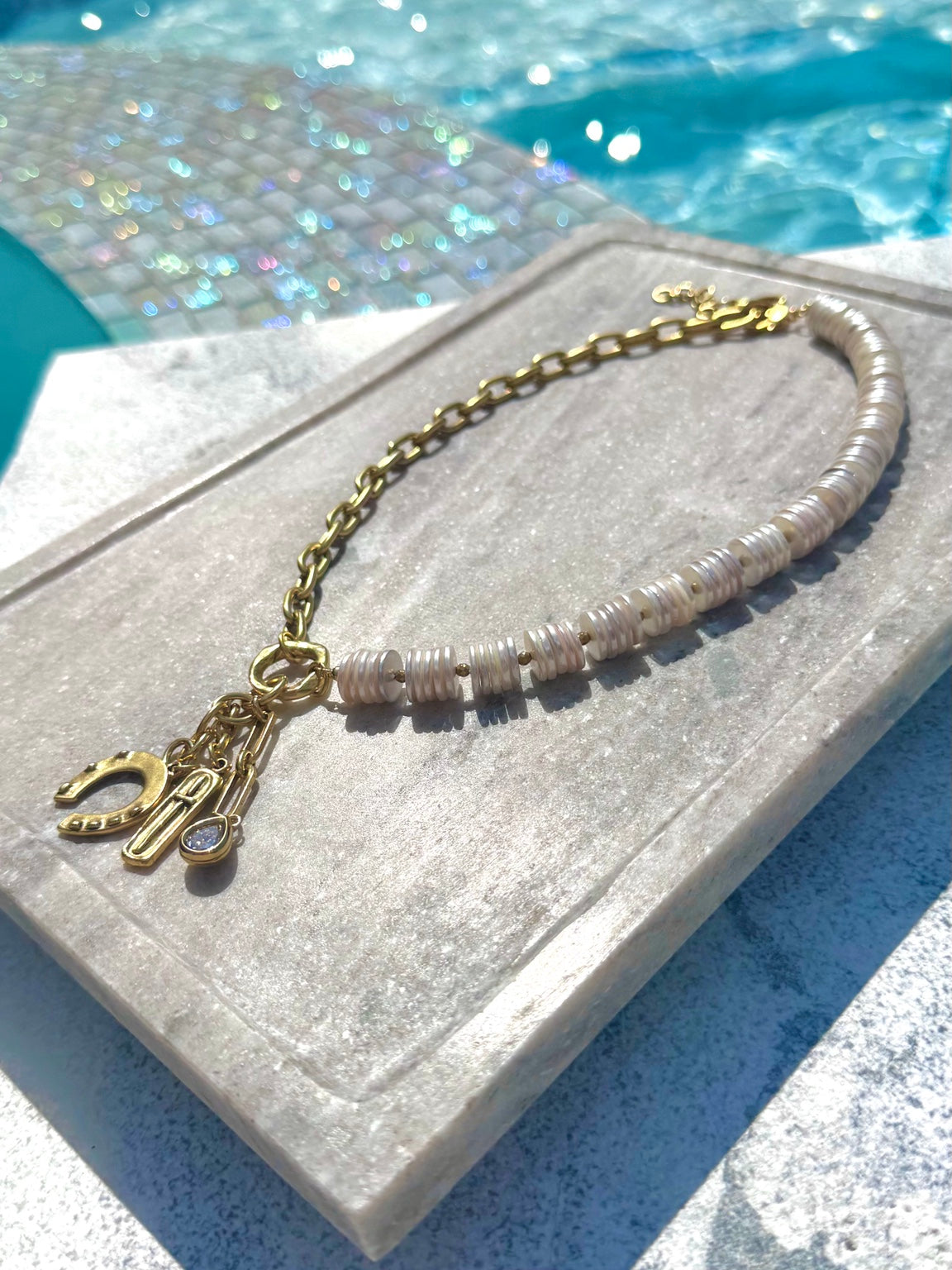 Angled poolside view of white shell disc and gold charm necklace