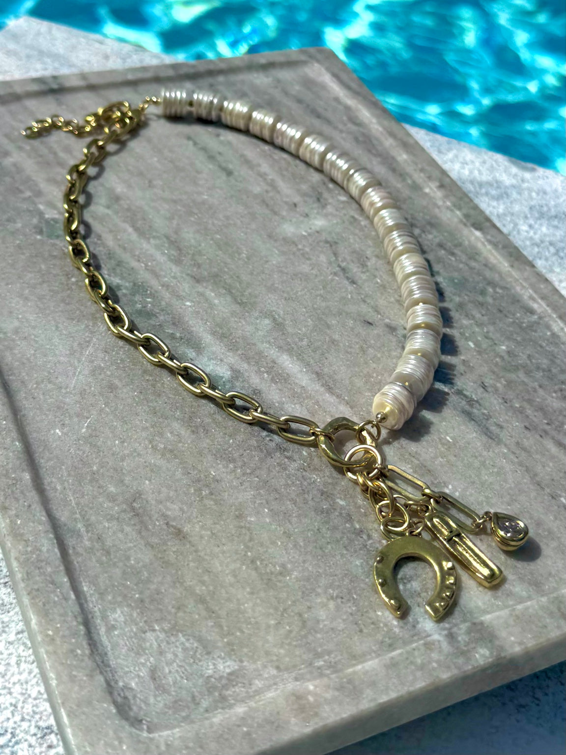 Close poolside view of shell disc and gold charm necklace