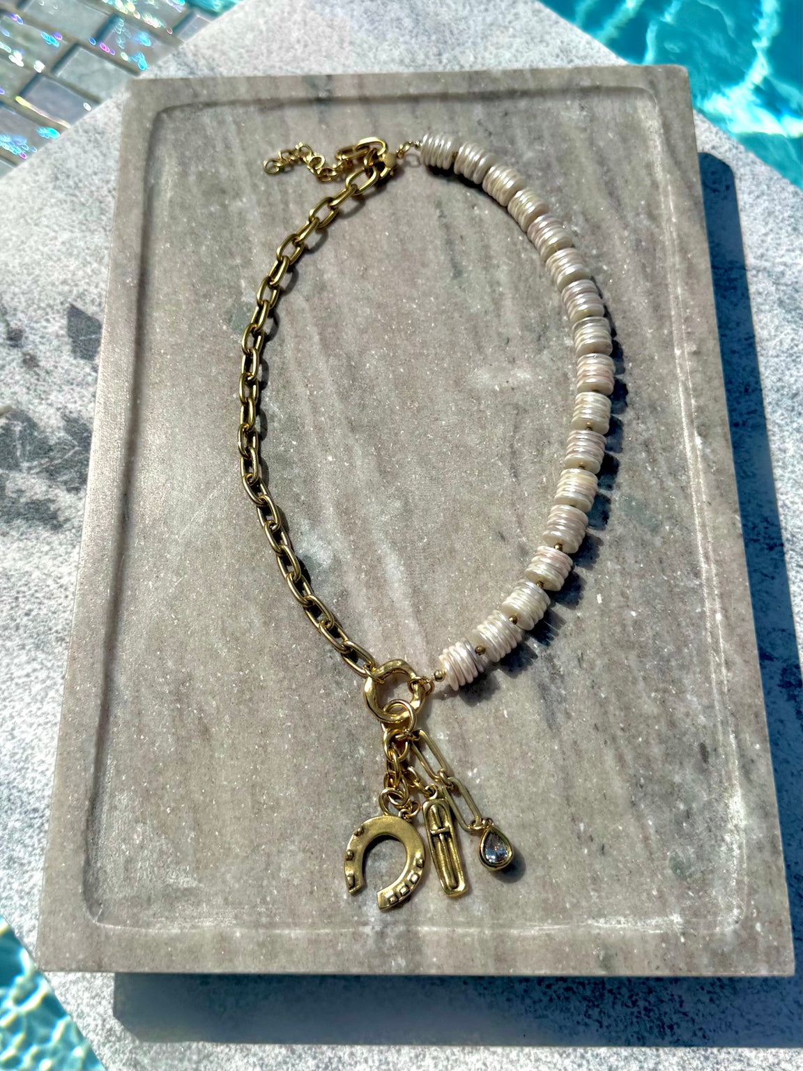 White shell disc and gold charm necklace photographed poolside