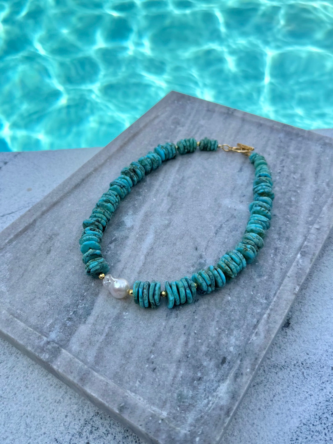 Angled poolside view of The Mackenzie dyed howlite and baroque pearl necklace