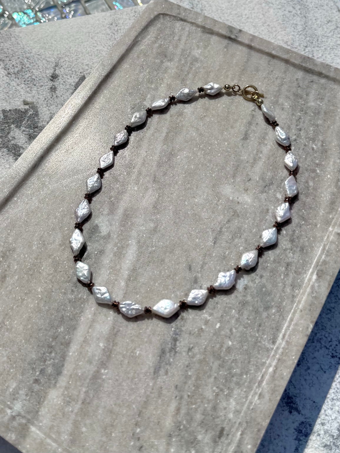 Angled poolside view of freshwater pearl and hematite necklace