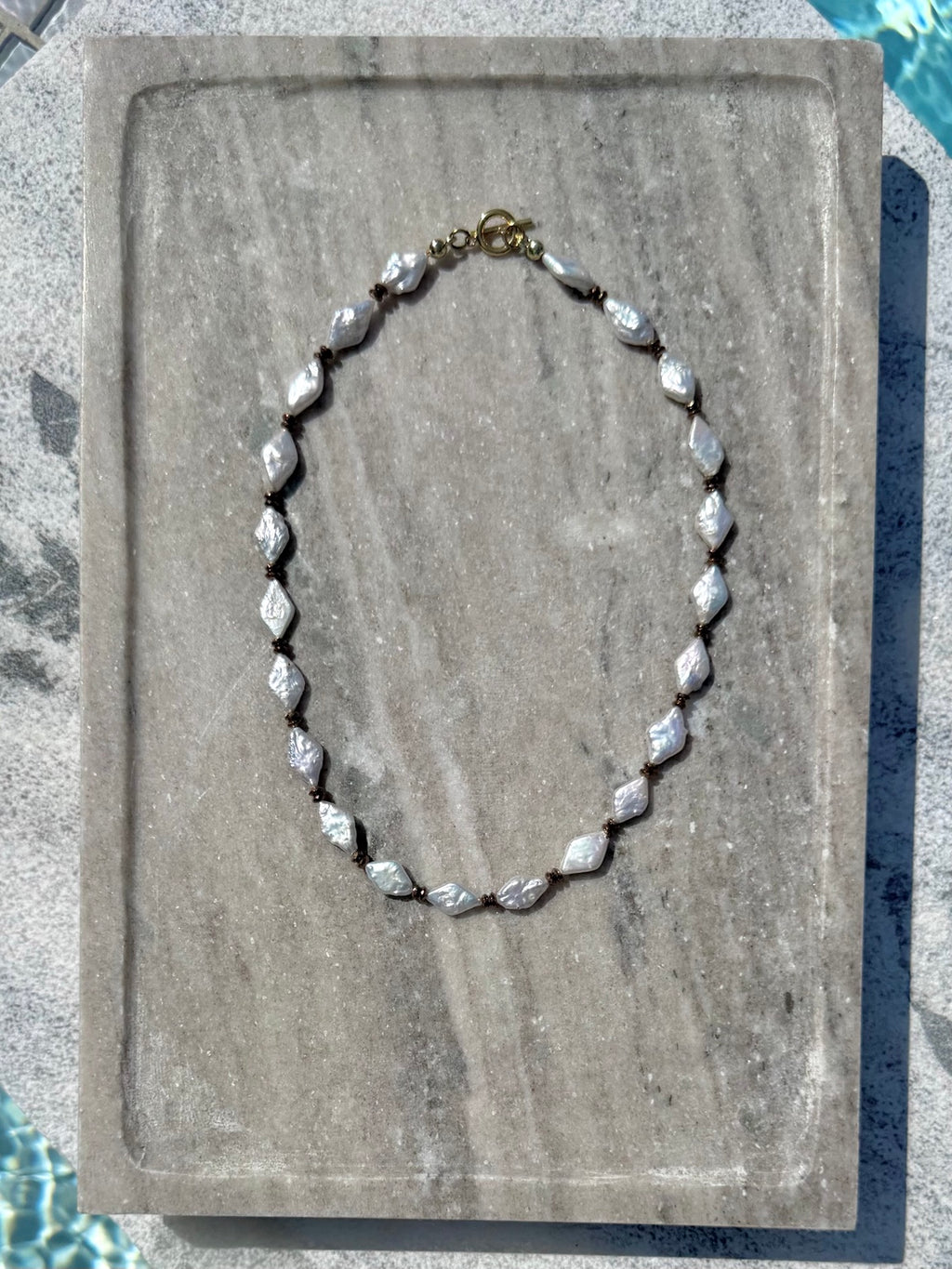 Full view of freshwater pearl and hematite necklace on stone tray
